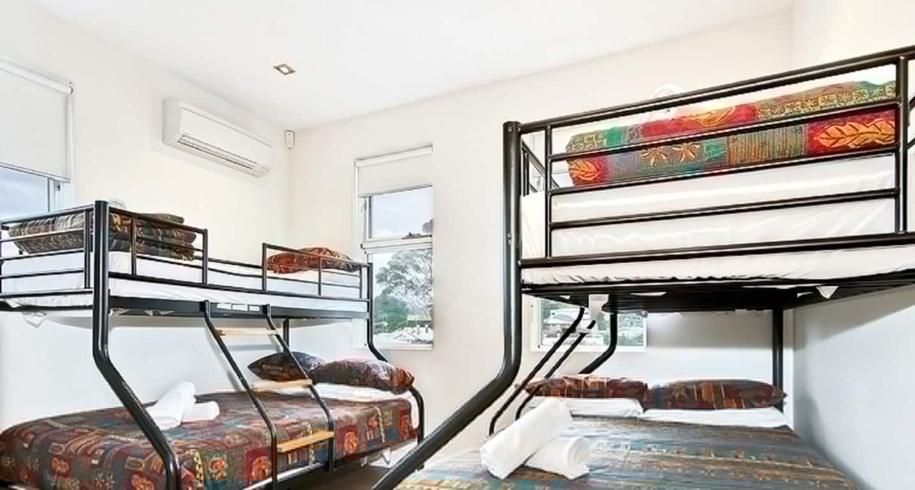 A dormitory room with bunk beds, a window, and an air conditioning unit.