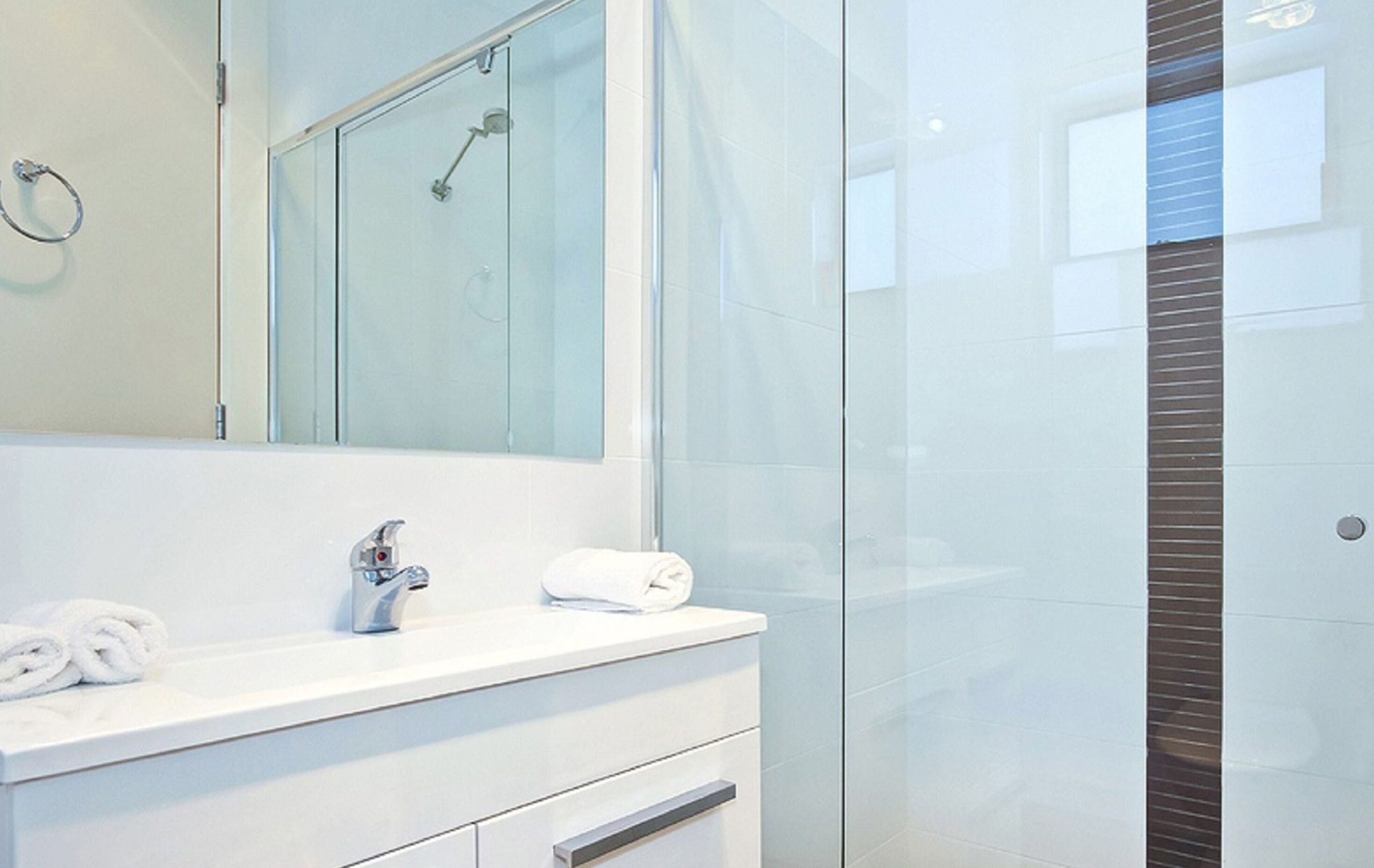 A modern bathroom with a glass shower enclosure, a white vanity with a mirror, and a towel on the counter.