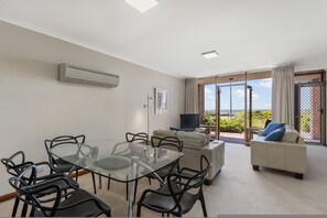 Un soggiorno moderno con un tavolo da pranzo in vetro, sedie nere, un divano beige e un televisore.