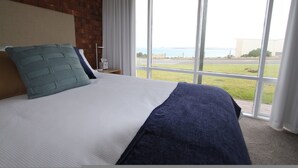 Habitación de hotel con una cama grande, vista al mar a través de una ventana y una pared de ladrillo.