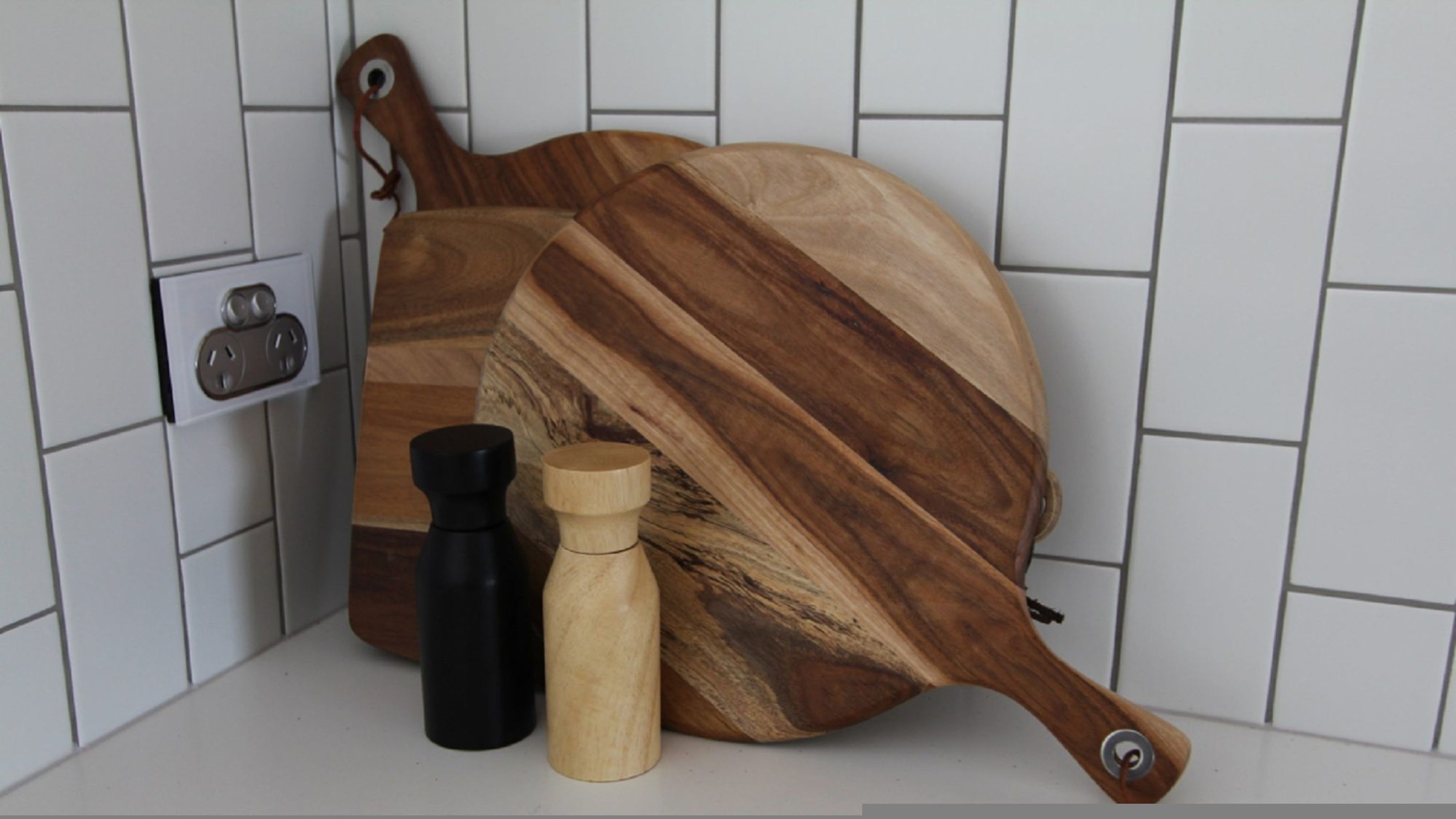 Un plan de travail de cuisine avec une planche à découper en bois, un moulin à poivre noir et un salière en bois.