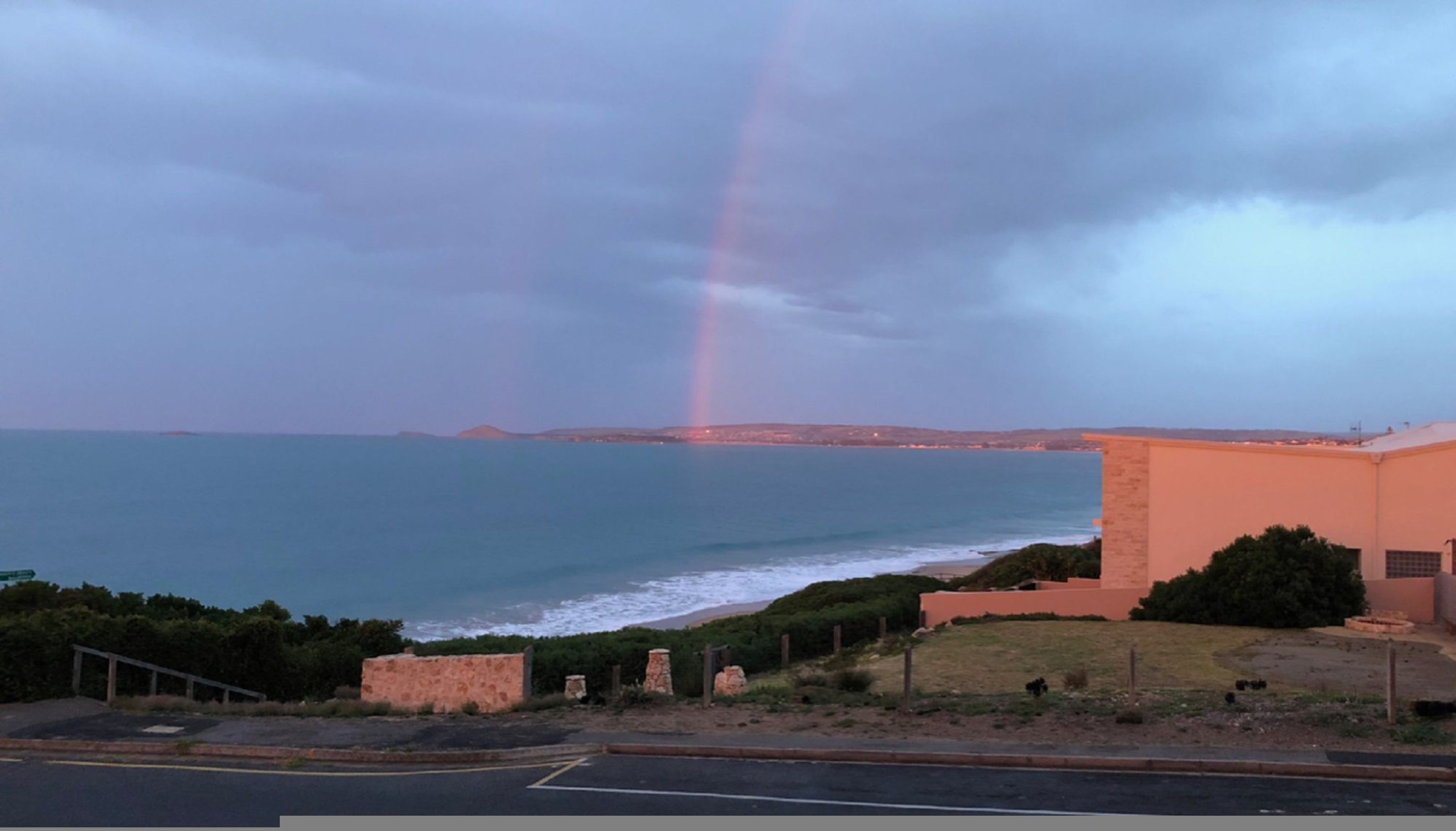 A coastal view with a rainbow, a building, and a road.