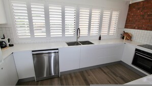Una cocina moderna con armarios blancos, lavavajillas de acero inoxidable, pileta doble y una pared de ladrillo decorativa.