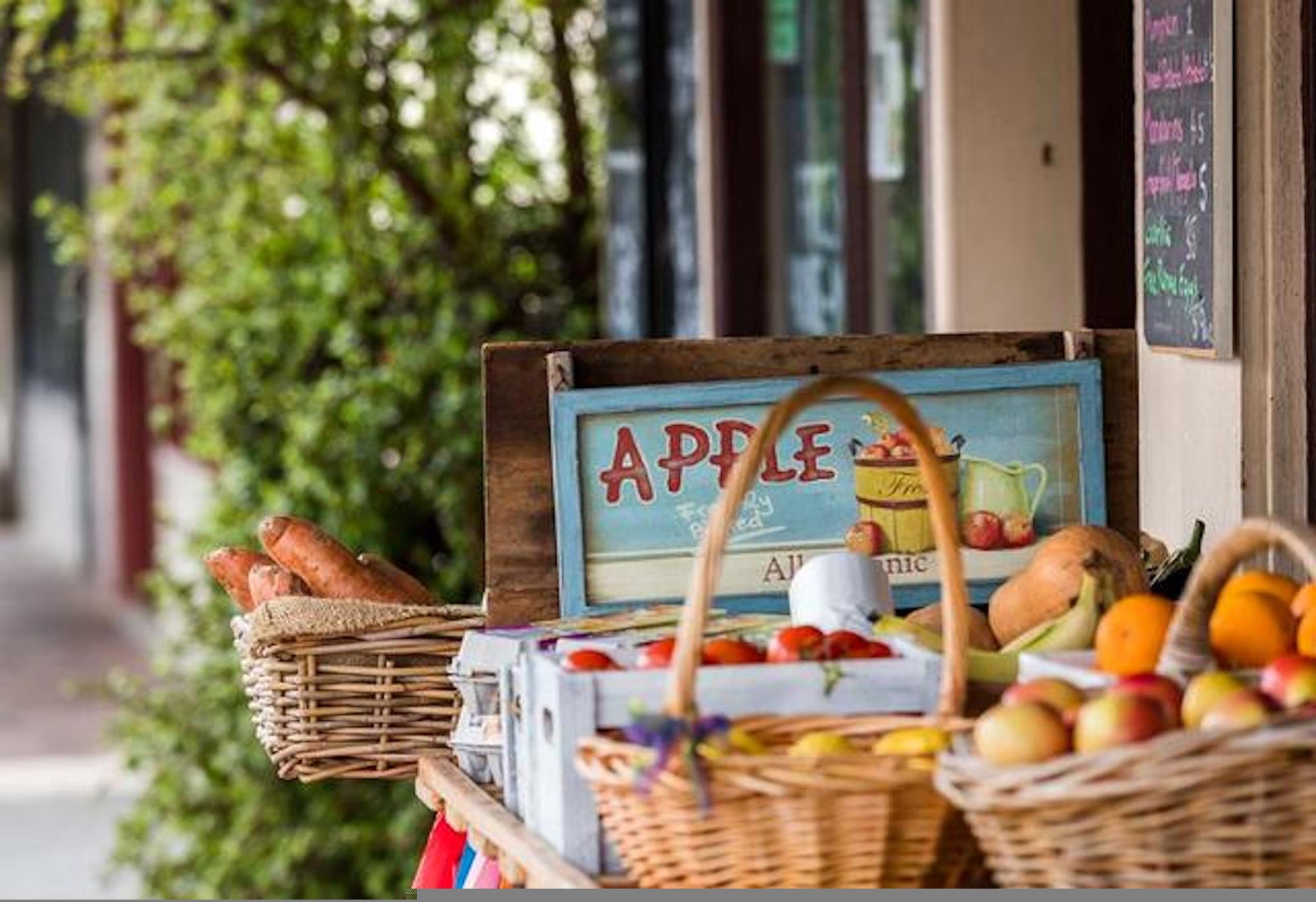 A fruit stand with a sign that reads "APPLE" and baskets of bread and fruit.