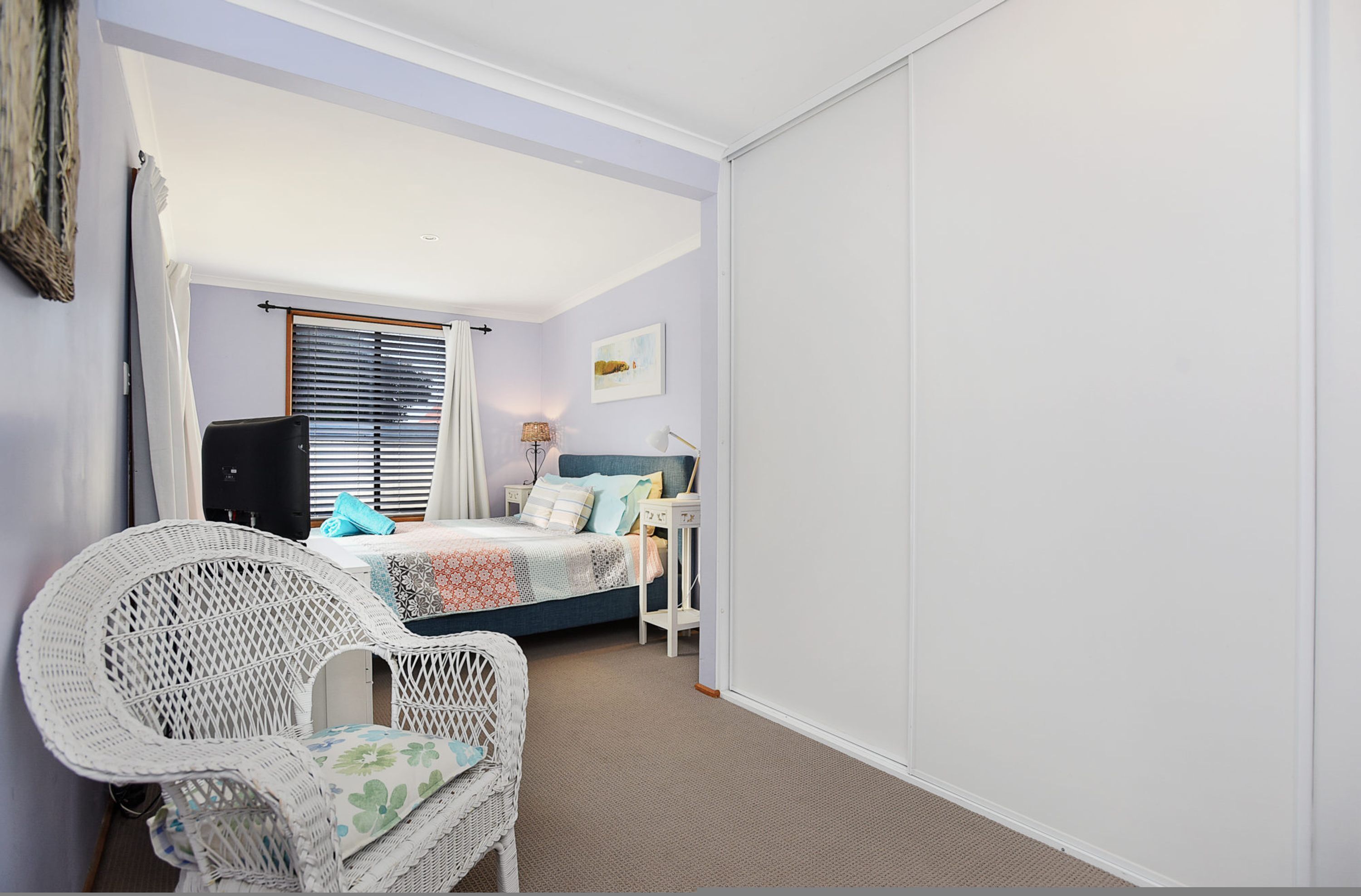 Un dormitorio con cama, una silla, una mesita de noche y una ventana con persianas.