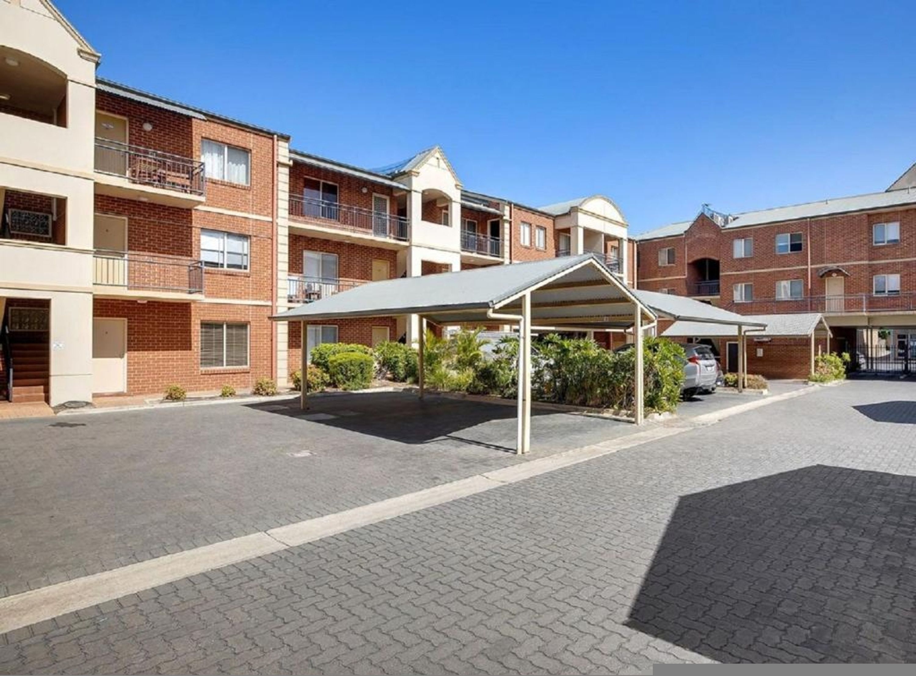 Un edificio residencial de varios pisos con un área de estacionamiento techada y un patio empedrado.