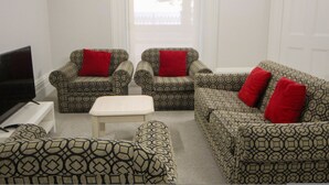 A living room with patterned furniture, a flat-screen TV, and a window with curtains.