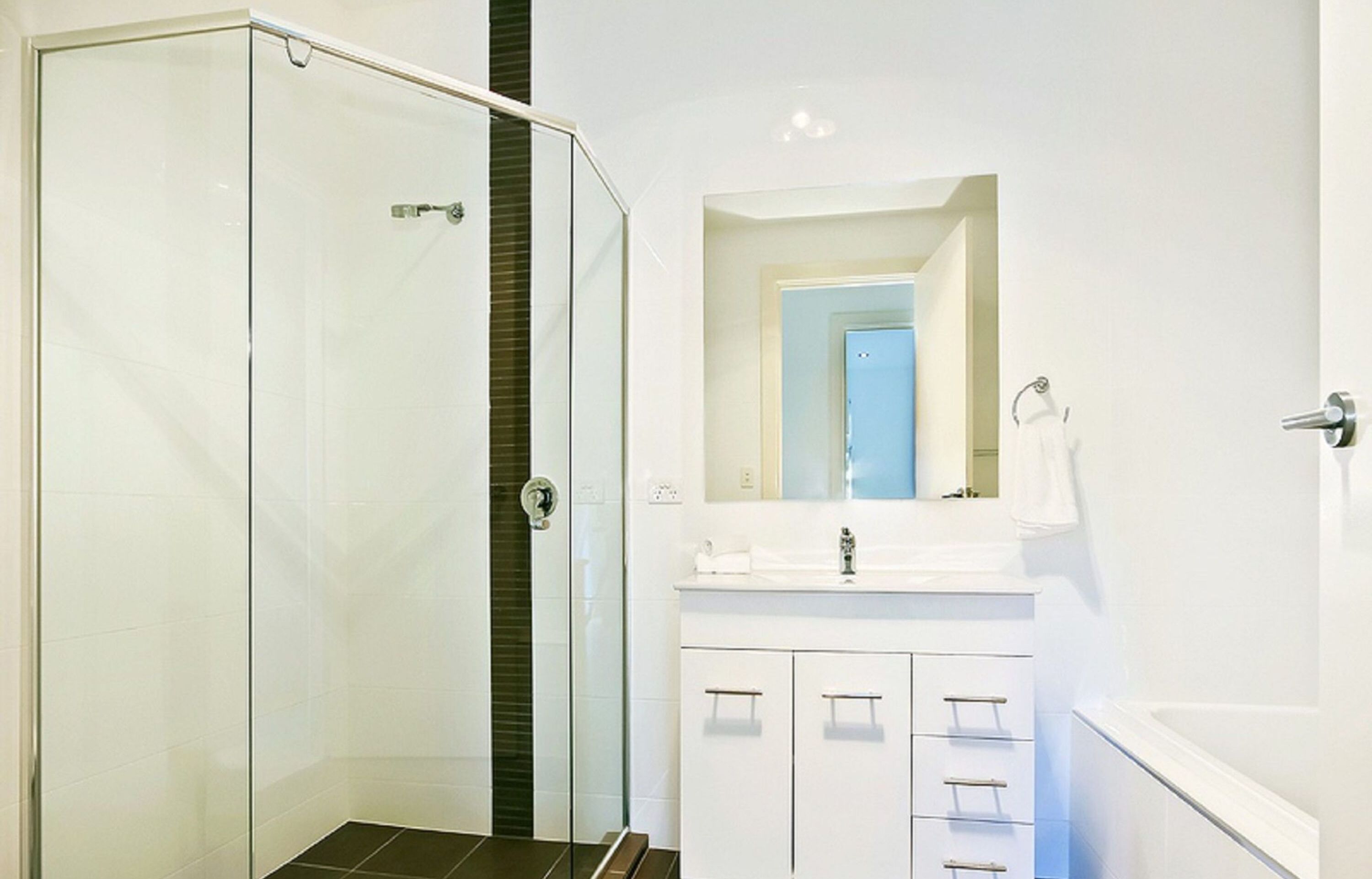 A modern bathroom with a glass shower enclosure, white vanity, and a large mirror.