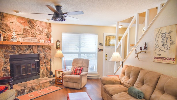A living room with a fireplace, a sofa, a chair, and a staircase. - The Red Chair Retreat at Red River (Red River)