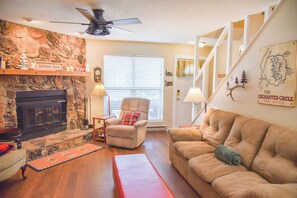 A living room with a fireplace, a sofa, a chair, and a staircase. - The Red Chair Retreat at Red River (Red River)