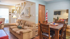 A living room with a sofa, a dining table with chairs, a staircase, and a television mounted on the wall. - The Red Chair Retreat at Red River (Red River)