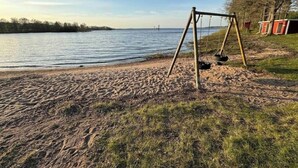 Une plage de sable avec une balançoire et, au fond, une rangée de cabanes rouges et blanches.