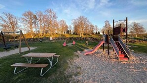 Une aire de jeux avec un toboggan, des balançoires et des tables de pique-nique.