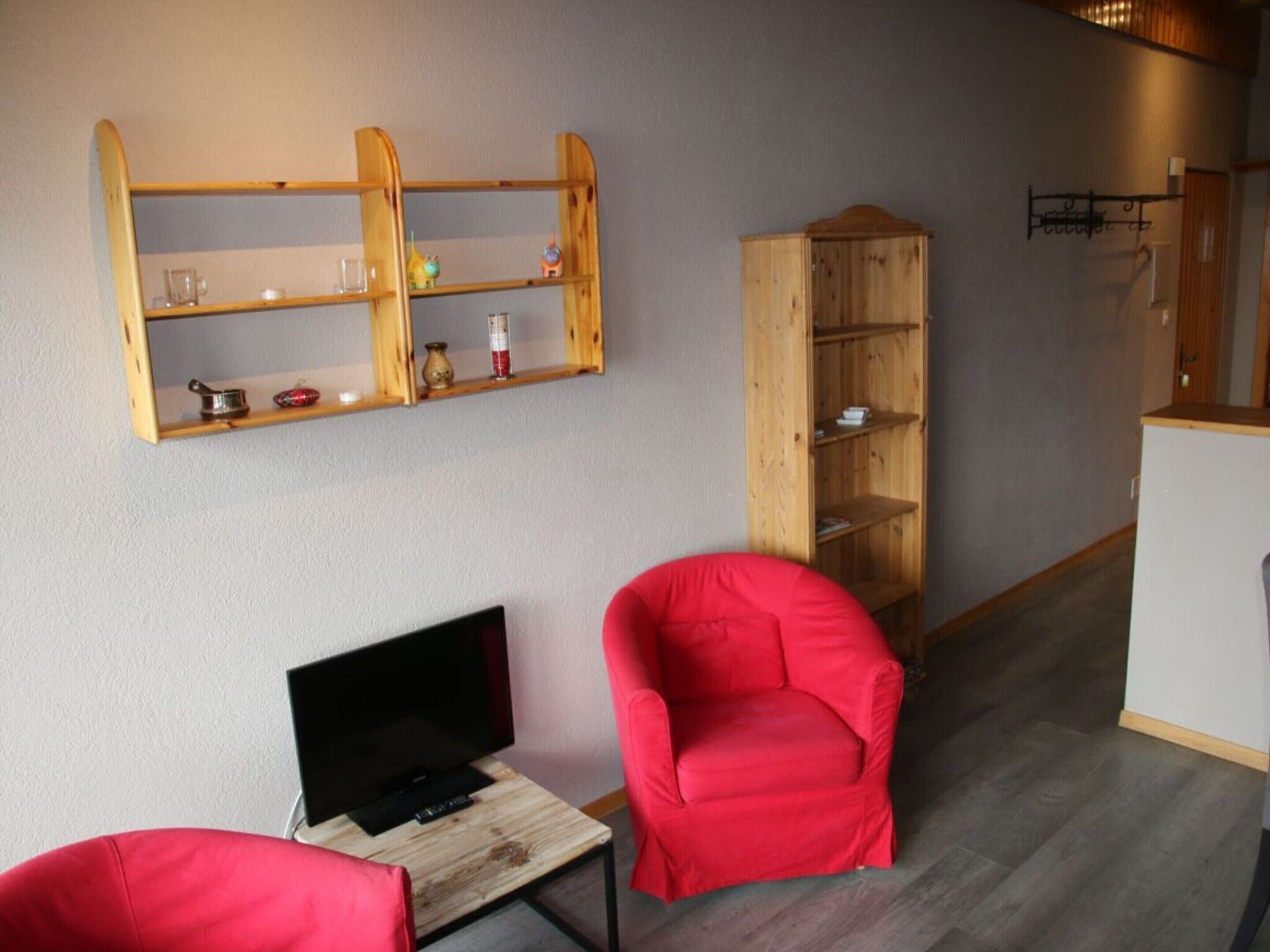 A room with a wooden TV stand, a red chair, and a wooden bookshelf against the wall.