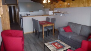 A cozy living area with a gray sofa, red armchairs, a wooden coffee table, and a dining table with chairs. A kitchen with a white refrigerator and a microwave is visible in the background. - Mystical Apartment With Mountain View (Veysonnaz)