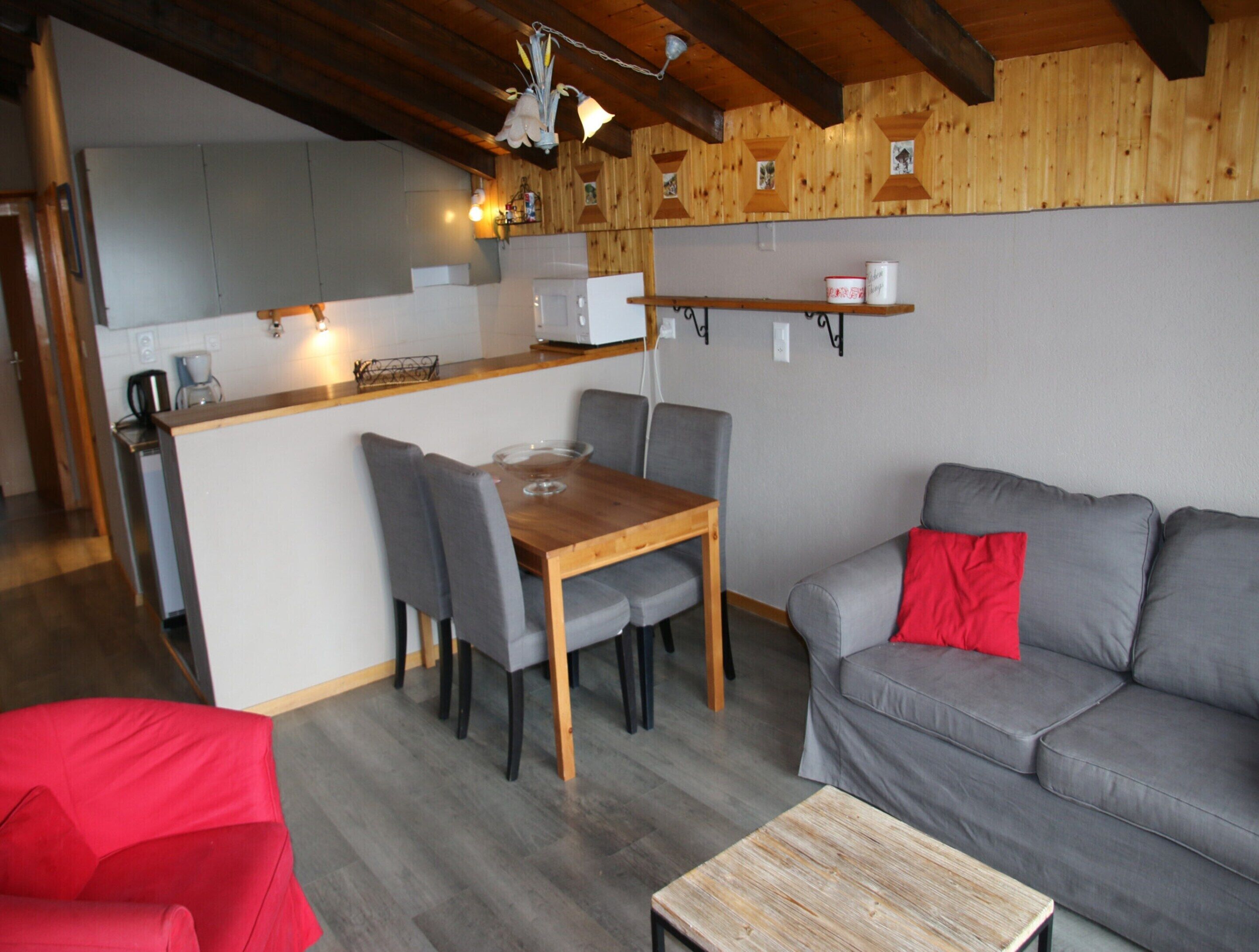 Ein gemütlicher Wohnbereich mit einem grauen Sofa, einem Holzesstisch und einem roten Sessel.