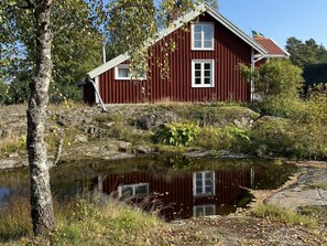 A red wooden house with a small porch and a pond in front. - 4 Person Holiday Home in Animskog (Ånimskog)