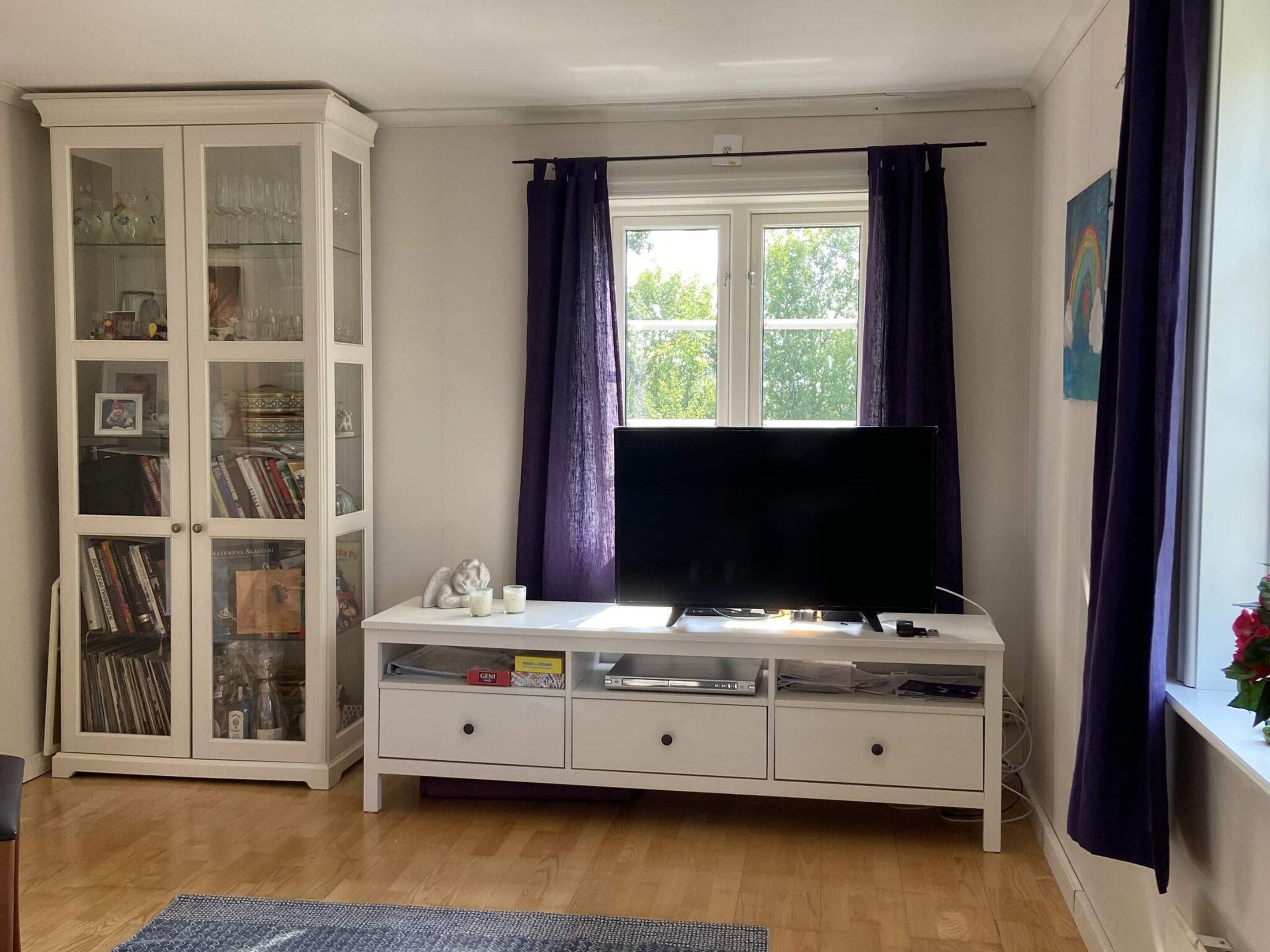 A living room with a white entertainment unit, a flat-screen TV, and a glass cabinet with books and decorative items.