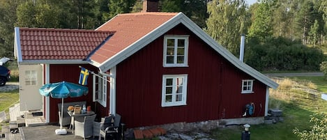Une maison rouge avec un toit en tuiles, une véranda avec des meubles d’extérieur et un drapeau.