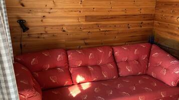 A wooden cabin interior with a red cushioned sofa against the wall.