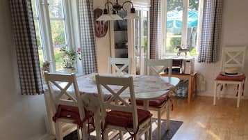 A dining area with a round table, white chairs, and a patterned tablecloth.