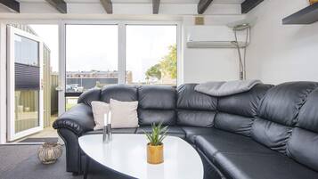 A modern living room with a black leather sectional sofa, a white coffee table, and a potted plant.