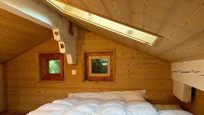 A wooden cabin room with a bed, two windows, and a sloped ceiling. - Chalet With Mesmerizing Mountain View (Veysonnaz)