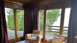 A cozy room with two leather armchairs, a wooden table, and large windows with plaid curtains. - Chalet With Mesmerizing Mountain View (Veysonnaz)