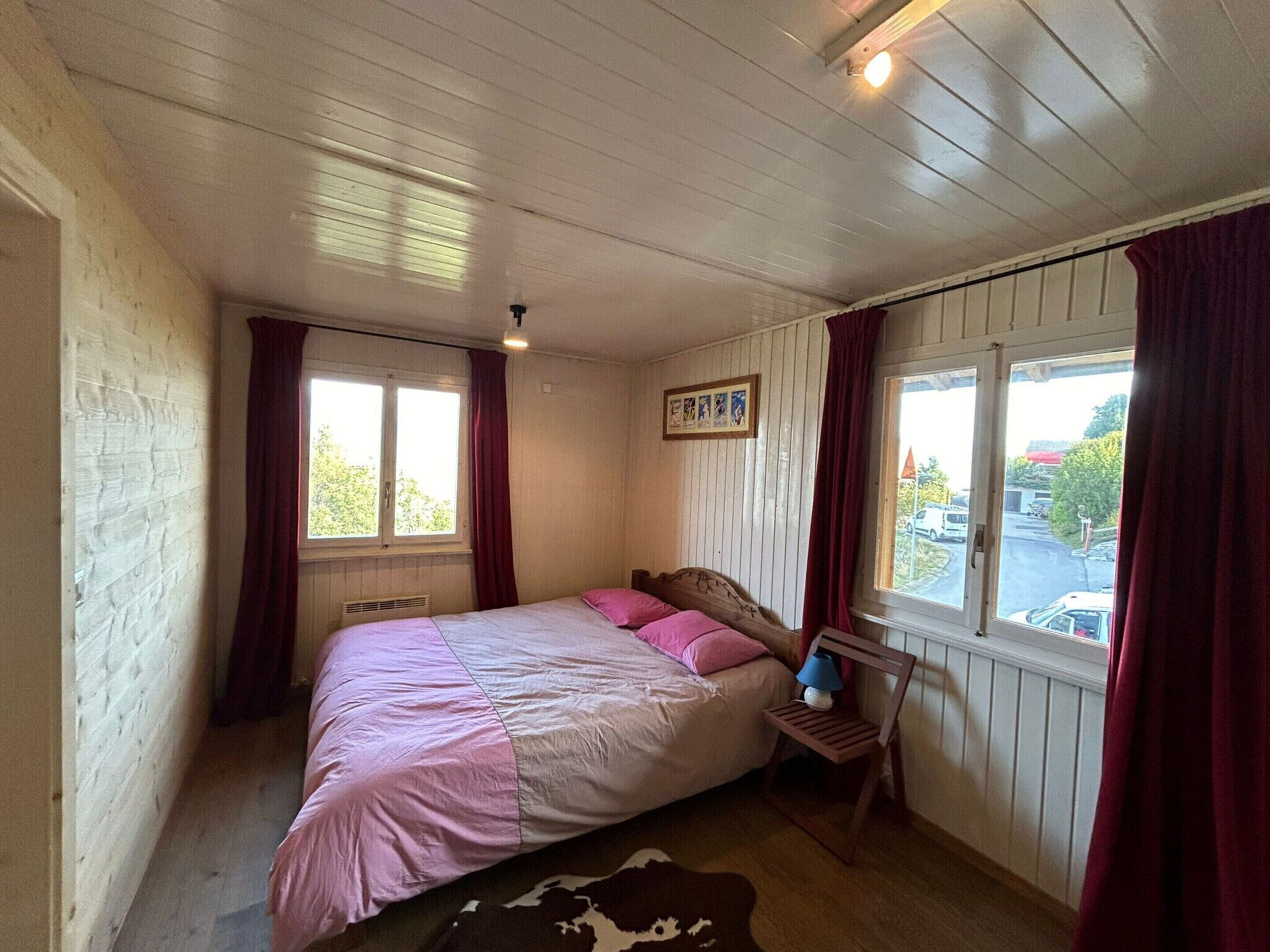 Un dormitorio con cama, ventana, radiador y una pequeña silla de madera.