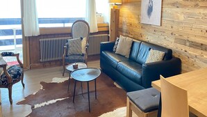 A cozy room with a wooden wall, a leather sofa, a chair, a small round table, and a cowhide rug. - Ski Lift Apartment With Views (Veysonnaz)