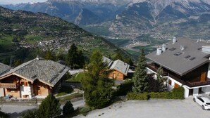 A mountain village with traditional wooden houses, a parking area, and a view of the surrounding mountains. - Apartment for Relaxed Vacation (Veysonnaz)