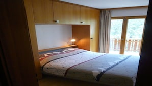 A bedroom with a bed, wooden cabinets, a nightstand, and a window with curtains. - Apartment for Relaxed Vacation (Veysonnaz)