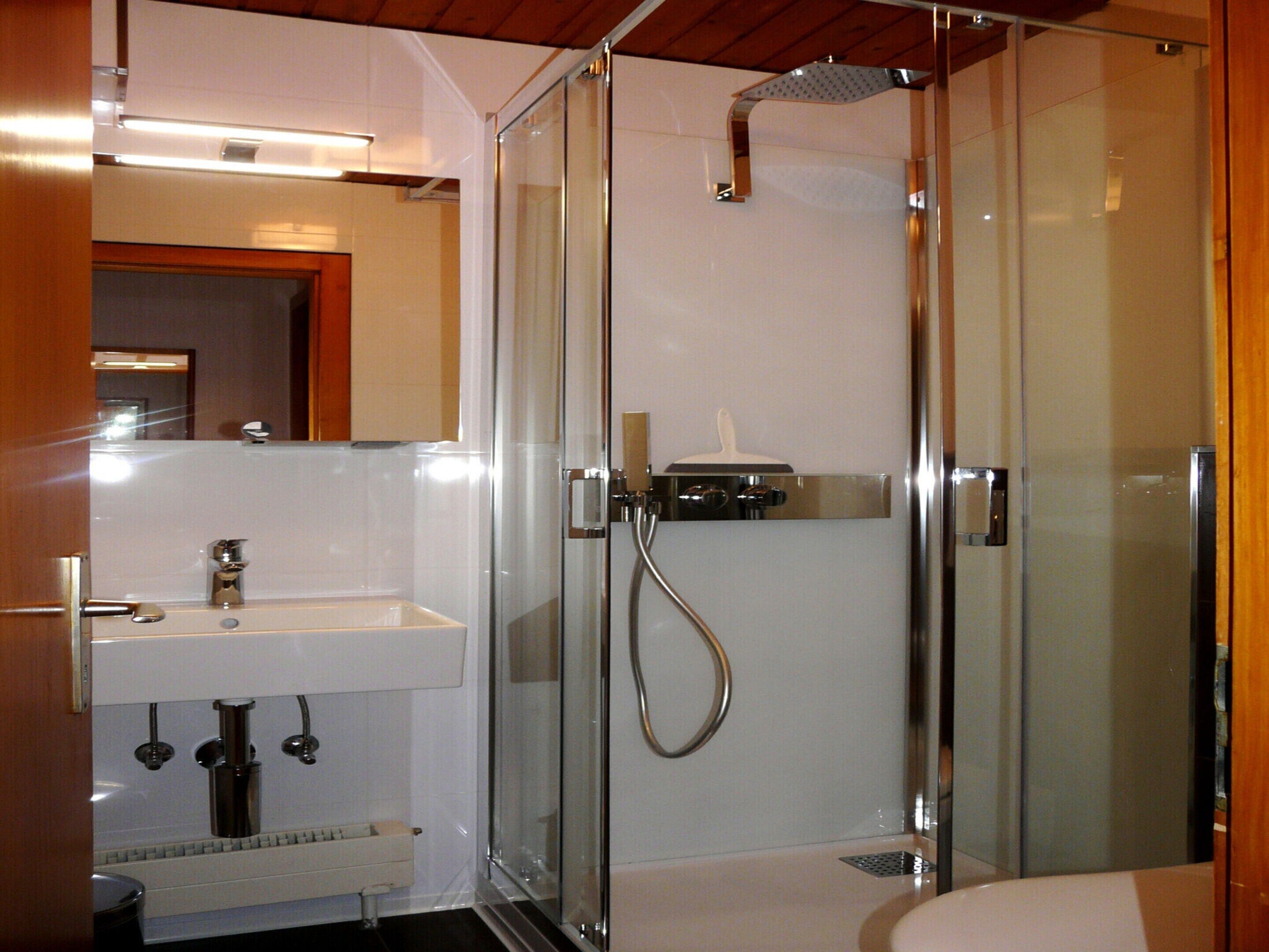 A modern bathroom with a glass-enclosed shower, a white sink, and a mirror above the sink.
