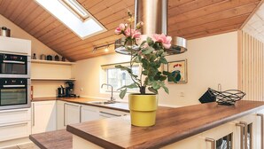 A modern kitchen with a wooden ceiling, skylight, stainless steel appliances, and a yellow planter with flowers.