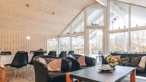 A spacious room with a high ceiling, wooden walls, and large windows offering a view of the outdoors.