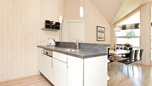 A modern kitchen with a built-in island, white cabinetry, and a large window providing natural light. - 5 Star Holiday Home in Grossenbrode (Grossenbrode)