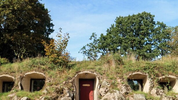 Conjunto de estructuras similares a cuevas con una puerta roja, rodeado de rocas y vegetación.