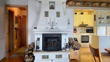 A living room with a fireplace, wooden flooring, and a kitchen area with modern appliances.