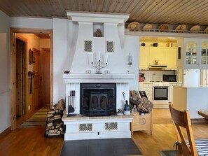 A living room with a fireplace, wooden flooring, and a kitchen area with modern appliances. - 4 Star Holiday Home in Amal (Åmål)