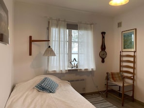 A bedroom with a bed, a chair, a lamp, a window with curtains, a clock, and a painting on the wall. - 4 Star Holiday Home in Amal (Åmål)