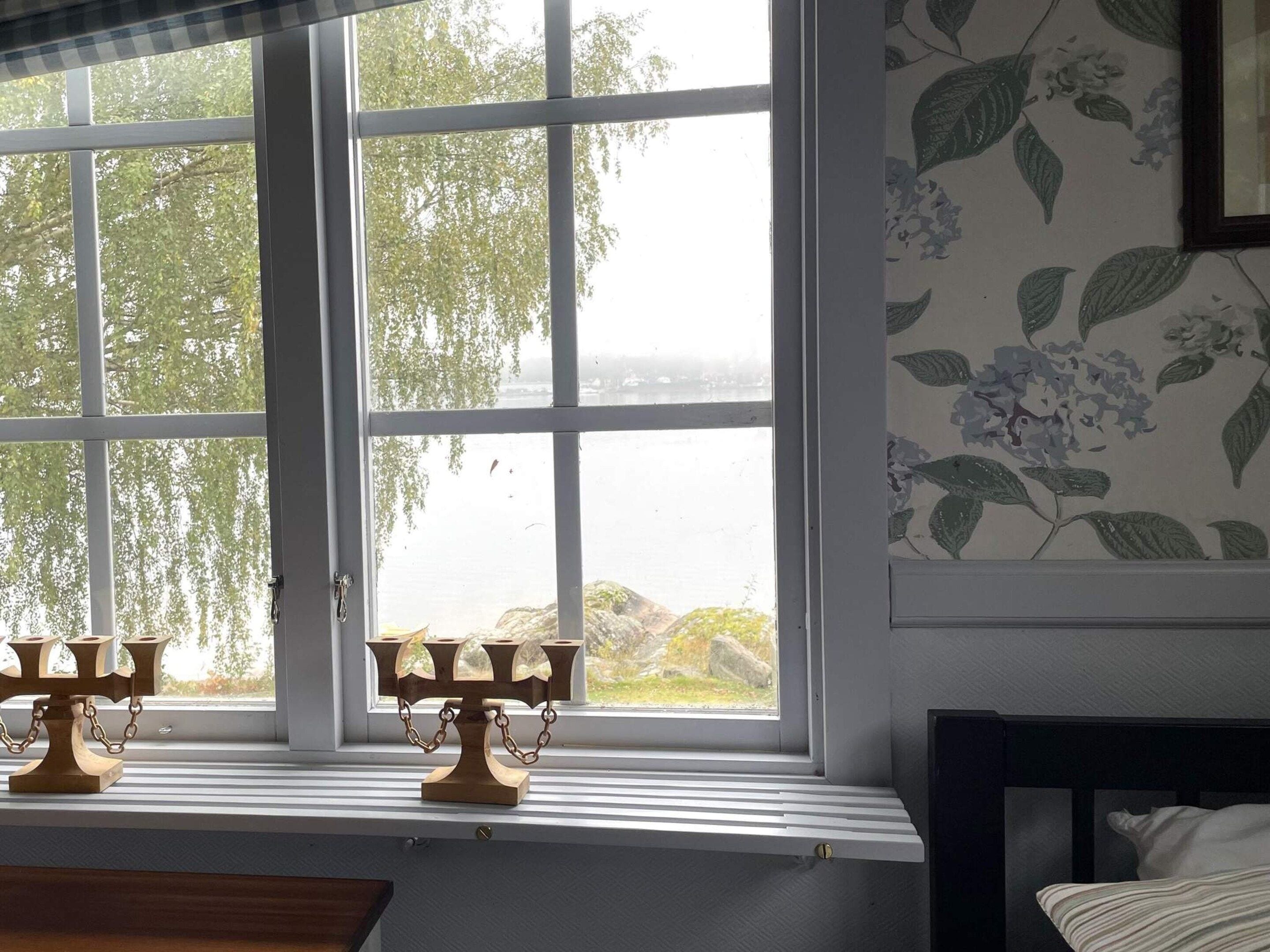 Una habitación con un ventanal grande, un candelabro de madera en el alféizar y una cama con almohada a rayas.