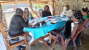 Un grupo de personas sentadas alrededor de una mesa con mantel azul, participando en una reunión.
