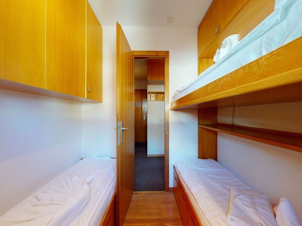 A narrow room with two bunk beds, wooden cabinets, and a small doorway leading to another room. - Apartment With Front Balcony (Nendaz)