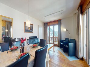 A dining area with a wooden table, chairs, and a view of a snowy landscape through a large sliding glass door. - Apartment With Front Balcony (Nendaz)