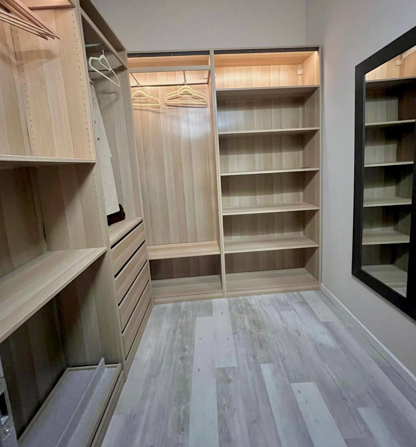 A walk-in closet with wooden shelves and a mirrored closet door.