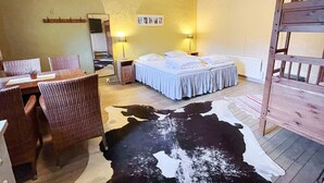 Una habitación con una cama, una mesa de comedor con sillas, un espejo y un tapiz de cuero de vaca.