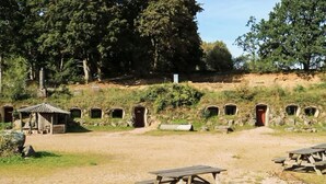 Un camping con mesas de picnic, un pequeño refugio y varias construcciones de piedra.