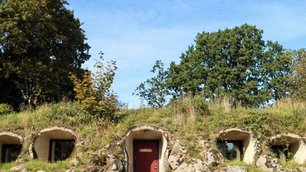 Una serie de construcciones de piedra con una puerta roja central, rodeadas de rocas y vegetación.