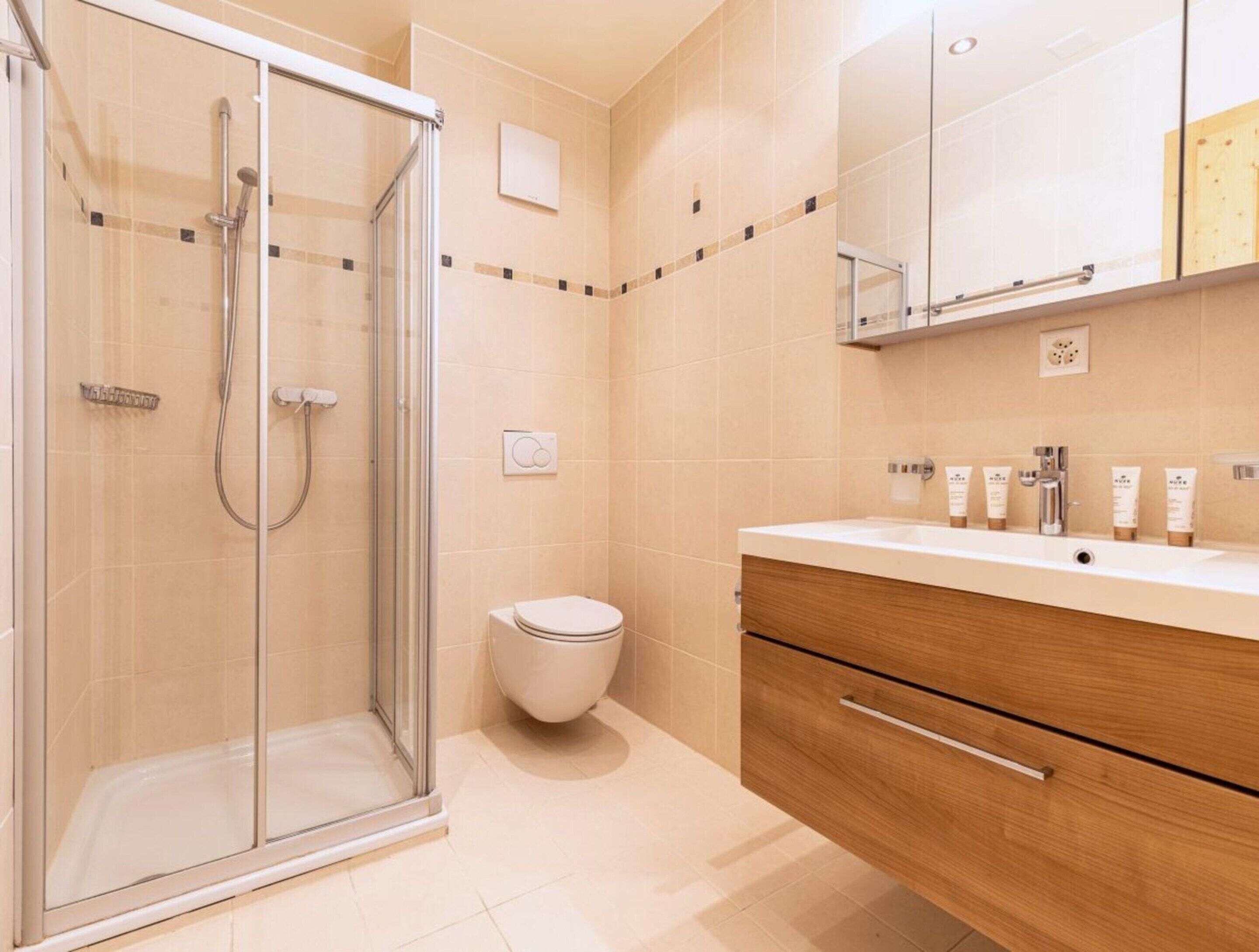 A modern bathroom with a glass-enclosed shower, a toilet, and a vanity with a mirror and toiletries.