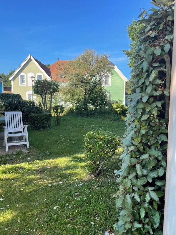 Un quartier résidentiel avec une maison à toit vert, une chaise blanche et une haie.